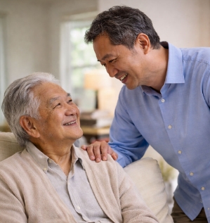 Adult son supporting an elderly father at home during a warm conversation.